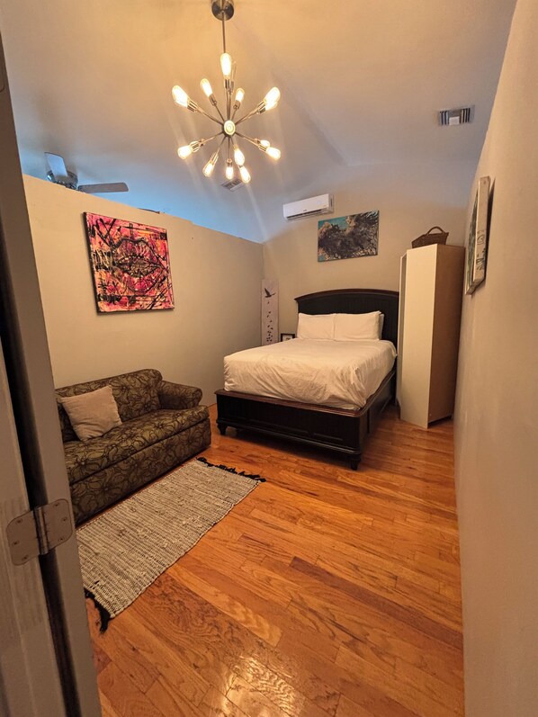 A bedroom with a bed, a sofa, a rug, a ceiling light fixture, and artwork on the walls.
