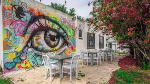 An outdoor seating area with tables and chairs, a mural with graffiti, and a building with windows. - THE ONLY HOUSE IN CHANNELSIDE BY WATER STREET (Tampa)