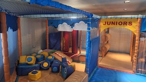 Espaço infantil com paredes de rede, estruturas de brincadeira acolchoadas e uma placa com a inscrição 'Juniors'.