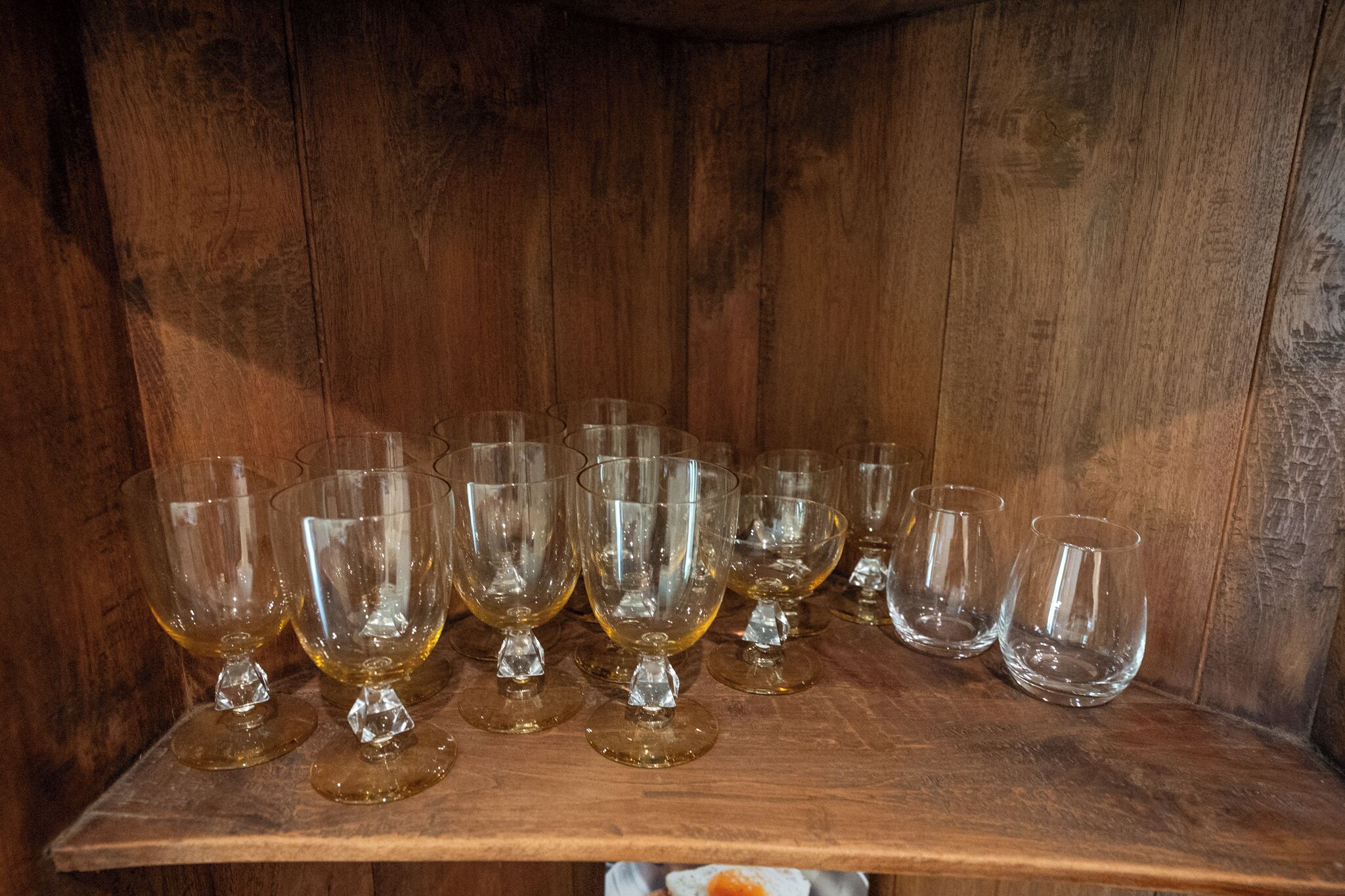 A wooden shelf with multiple clear glass goblets.