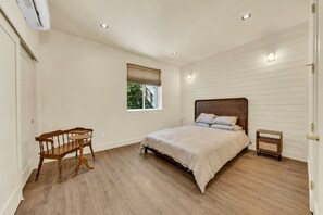 Een slaapkamer met een bed, een houten stoel, een klein tafeltje en een raam met jaloezieën.