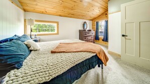 Un dormitorio con techo de madera, una cama con manta tejida, un aparador y una ventana.