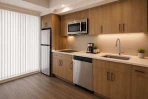 A modern kitchen with wooden cabinets, stainless steel appliances, a dishwasher, and a coffee maker. - Norvian Urban Suites (Toronto)