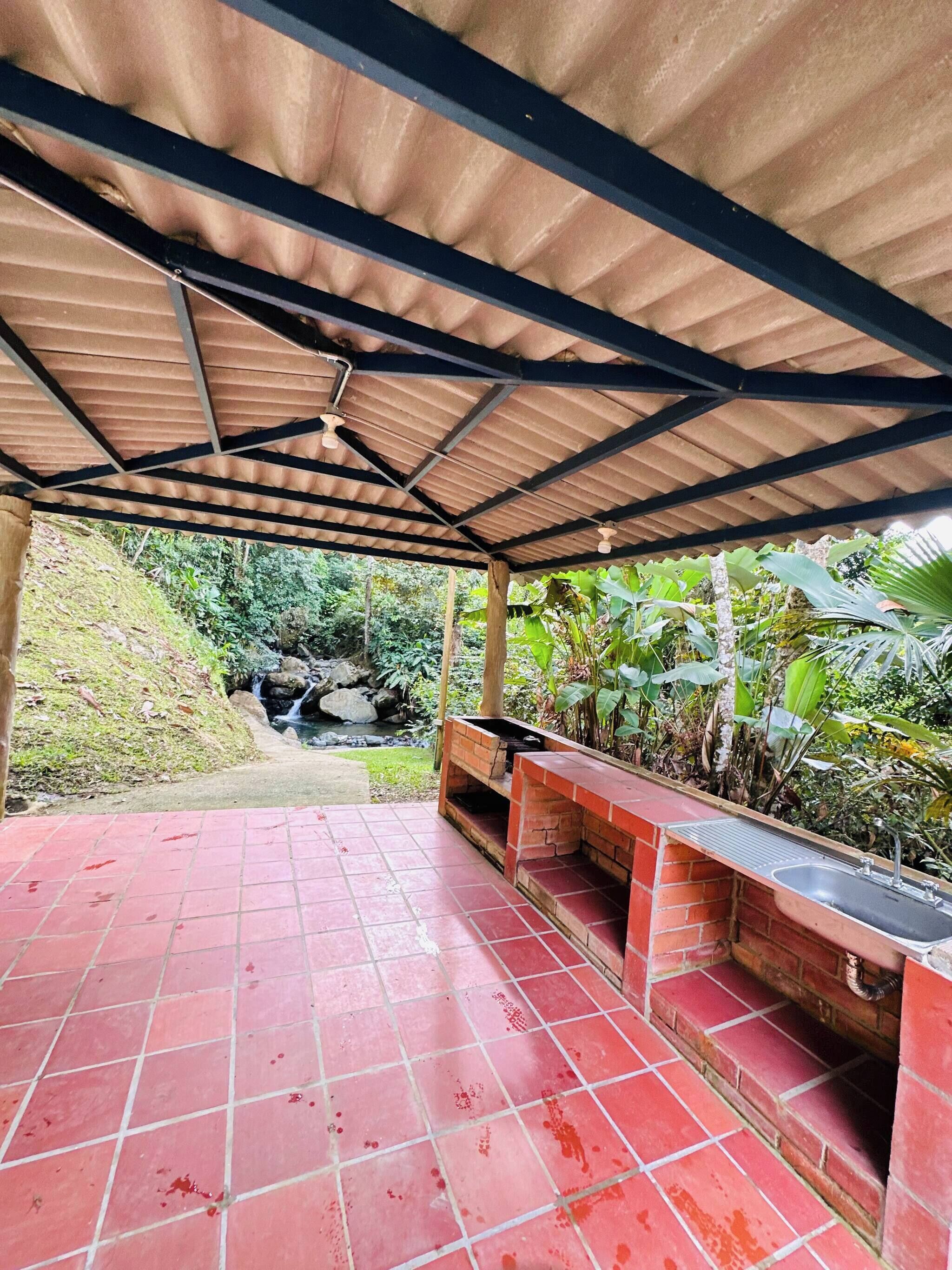 A covered patio area with a brick barbecue and a sink.