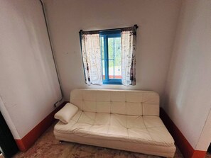 Ein Eckzimmer mit einem beigefarbenen Sofa, einem Fenster mit gemusterten Vorhängen und Blick auf Grünflächen.