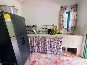 Eine Küche mit Kühlschrank, Spüle, einem Fenster mit Vorhängen und einer gefliesten Spritzschutzwand.
