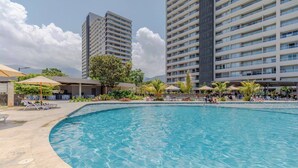 A swimming pool with lounge chairs and umbrellas, surrounded by tall buildings. - Apartament with view at the sea close at the airport (Urb Don Jaca)