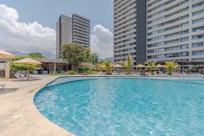 A swimming pool with lounge chairs and umbrellas, surrounded by tall buildings. - Modern Beachfront Loft in Santa Marta (Urb Don Jaca)