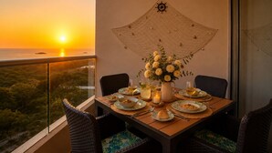 A dining table with plates, glasses, and a candle, set against a sunset view. - Apartament with view at the sea close at the airport (Urb Don Jaca)
