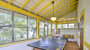A room with a ping pong table, large windows, and a yellow ceiling. - Historic Home on Beaver Dam Lake w/ Seasonal Dock (Cumberland)