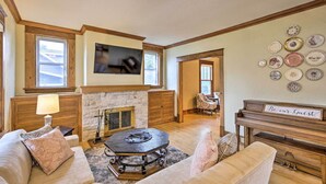 A cozy living room with a fireplace, a piano, and a wall decorated with plates. - Historic Home on Beaver Dam Lake w/ Seasonal Dock (Cumberland)