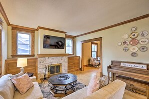 A cozy living room with a fireplace, a piano, and a wall decorated with plates. - Historic Home on Beaver Dam Lake w/ Seasonal Dock (Cumberland)