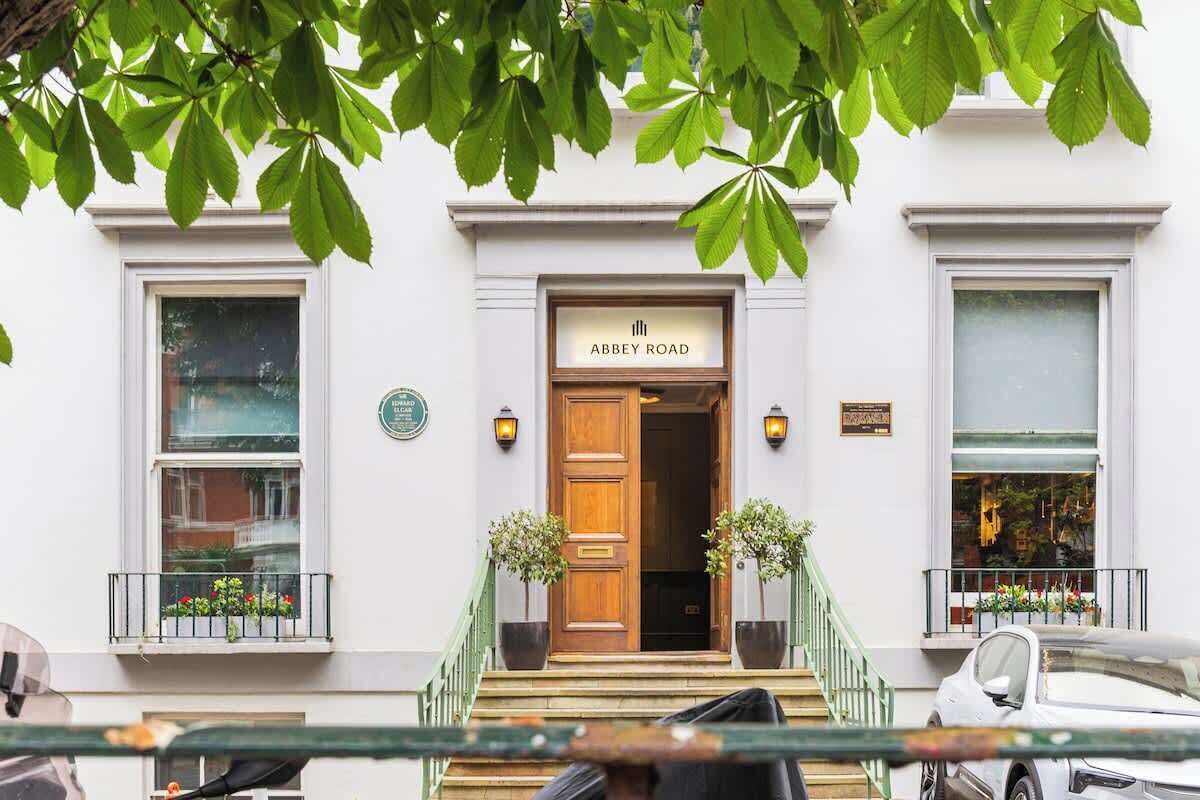 Un bâtiment avec une enseigne indiquant « Abbey Road » à l’entrée, un escalier menant à la porte et une voiture garée devant.