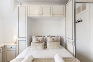 Ein Schlafzimmer mit einem Bett, Kissen, einem Nachttisch, einer Lampe und einem Kleiderschrank.