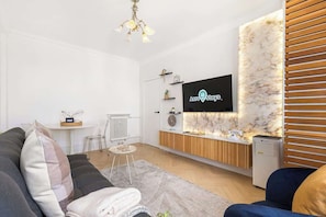Ein modernes Wohnzimmer mit einer Couch, einem Couchtisch, einem an einer Marmorwand befestigten Fernseher und einer kleinen Küchenzeile mit einem Kühlschrank.