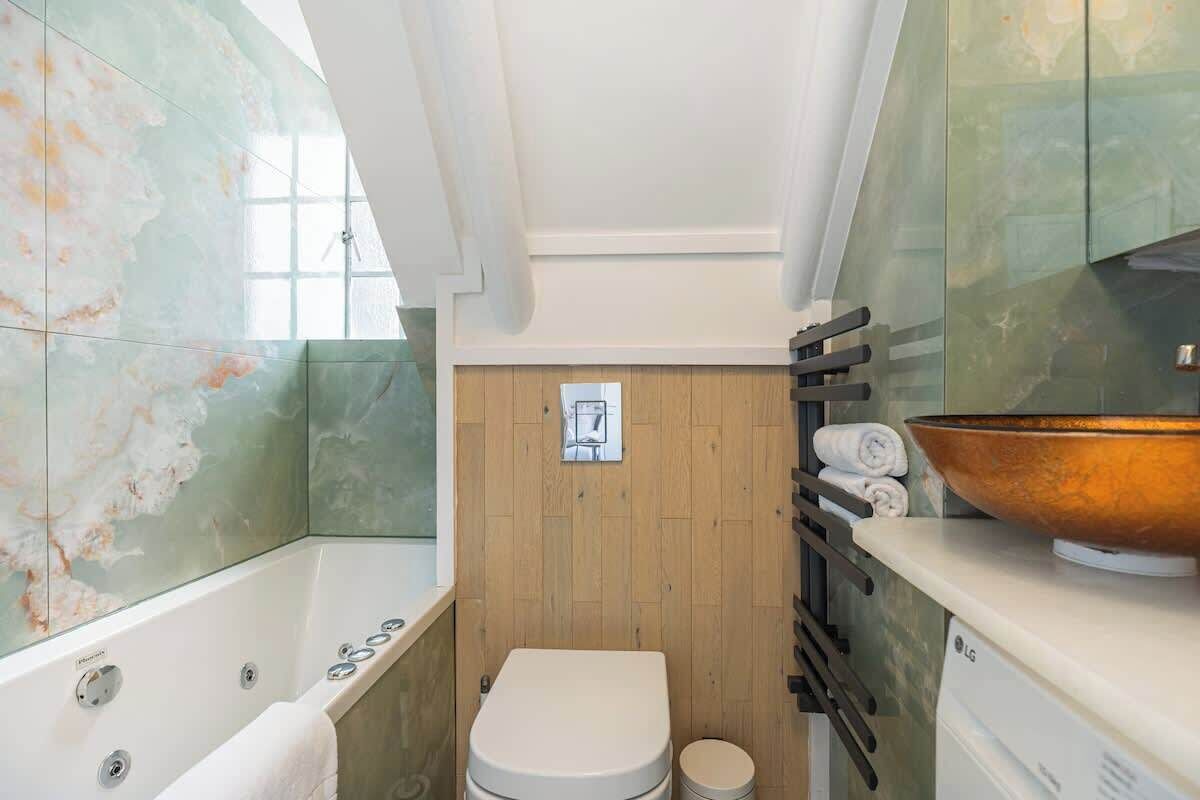 Ein Badezimmer mit Badewanne, Toilette und Waschbecken, mit einer Holzwand und einem großen Spiegel.