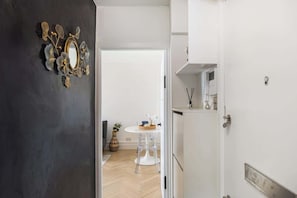 Ein Durchgang zu einem Raum mit einer weißen Tür, einem Spiegel mit floralen Verzierungen, einem kleinen Tisch mit einer Vase und einem weißen Schrank.