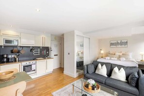 Ein modernes Hotelzimmer mit Küchenzeile, einer Couch, einem Bett und einem Glastisch.