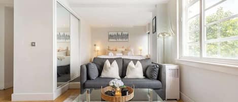 A modern living room with a glass coffee table, grey sofa, and a large window.