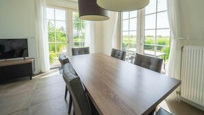 A modern dining room with a large table, chairs, a TV, and large windows with curtains. - Holiday Home in Uitdam With Sauna (Uitdam)