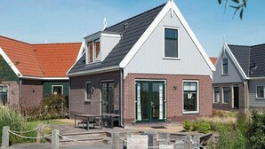A modern house with a sloped roof, a brick facade, and a wooden deck with outdoor seating. - Holiday Home in Uitdam With Sauna (Uitdam)