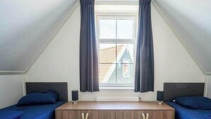 A room with two beds, a window with curtains, a radiator, and a wooden cabinet. - Holiday Home in Uitdam With Sauna (Uitdam)