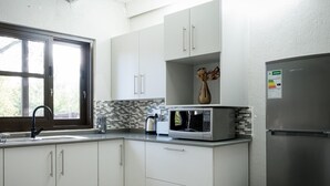 Une cuisine moderne avec des meubles blancs, un réfrigérateur en acier inoxydable, un four à micro-ondes et une fenêtre donnant sur un paysage verdoyant.