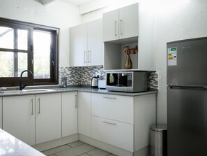 Een moderne keuken met witte kastjes, een roestvrijstalen koelkast, een magnetron en een raam met uitzicht op groen.