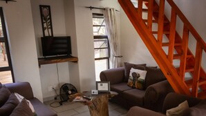 Un salon avec un canapé marron, une table basse en bois, un téléviseur fixé au mur et un escalier en bois.