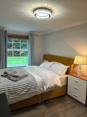 Een slaapkamer met een bed, nachtkastje, lamp en een raam met gordijnen.