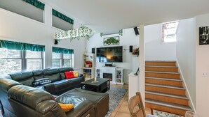 Una sala de estar con un sofá de cuero, televisor, chimenea y una escalera.