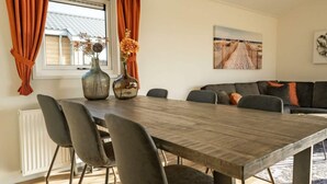 A dining area with a wooden table, grey chairs, and a grey sofa. There are two vases with flowers on the table. - Velthorst Waterfront 6 (Linden)