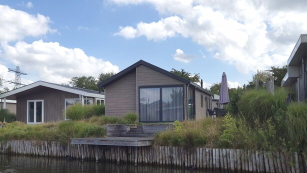 A modern house with a large sliding glass door, a deck, and a view of a body of water. - Velthorst Waterfront 6 (Linden)