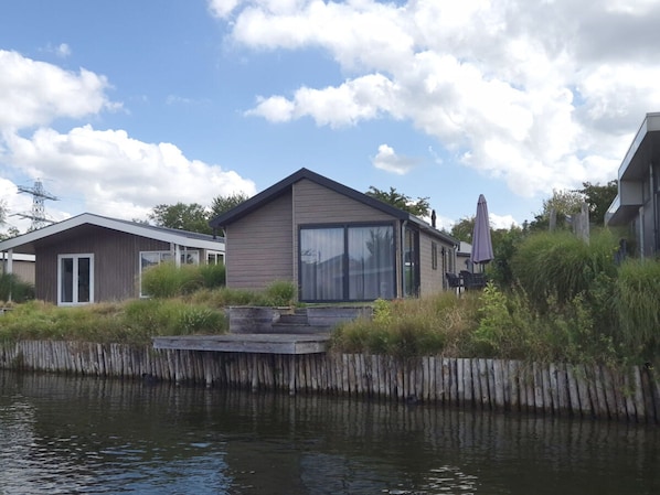 Ein modernes Haus mit einem großen Schiebeglastür, einer Terrasse und Blick auf ein Gewässer.