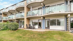 Un edificio residencial de varios pisos con balcones, un patio con mobiliario exterior y un césped bien cuidado.