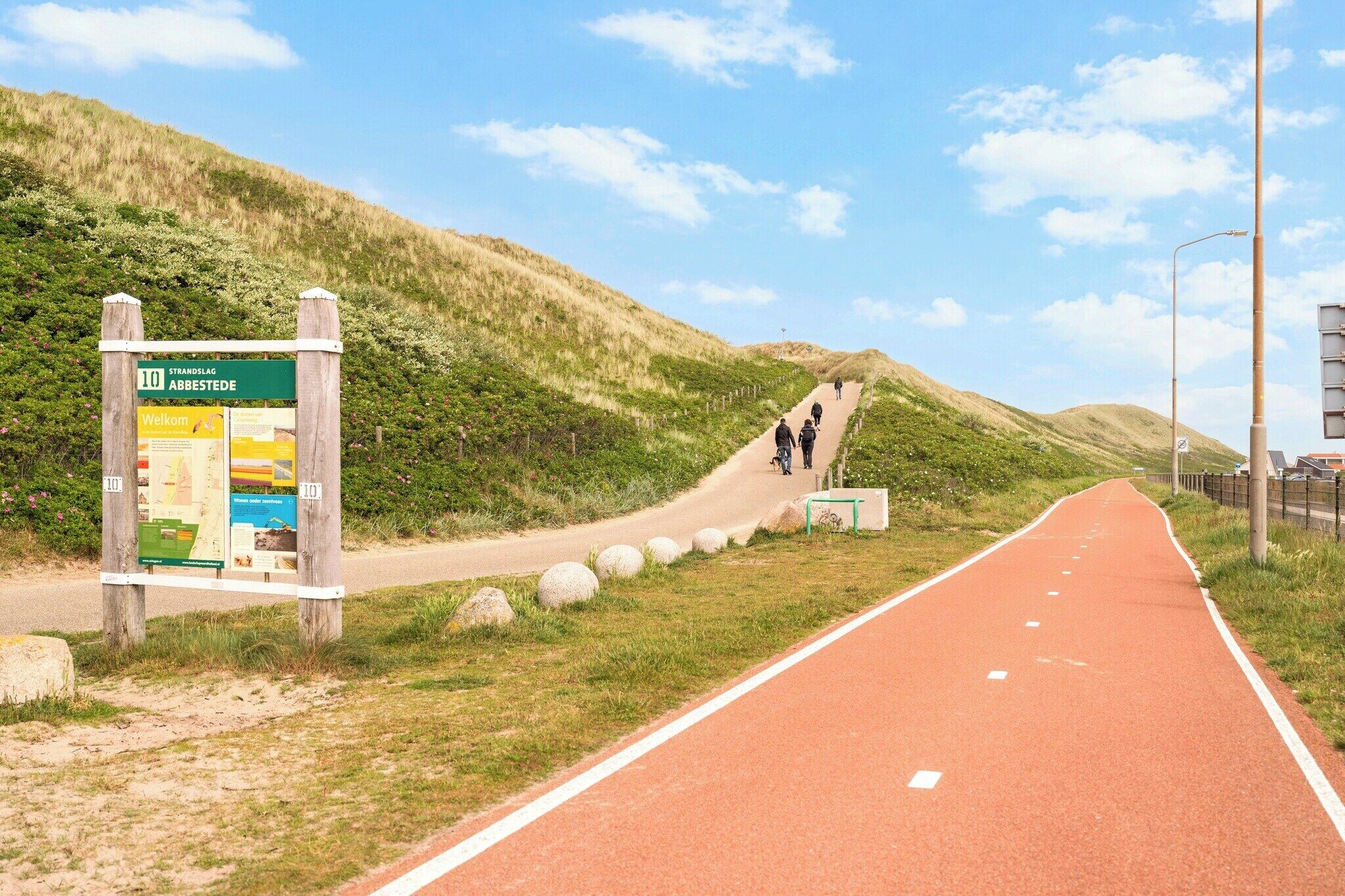 Un chemin pavé, avec un panneau indicateur et une colline verdoyante en arrière-plan.