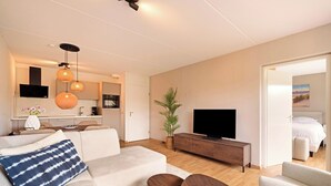 Una sala moderna con sofá, mesa de centro, televisor y zona de comedor con cocina al fondo.