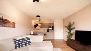 Una sala de estar moderna con un sofá, un televisor y un comedor con una cocina al fondo.