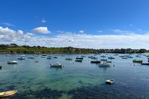 Eine Küstenbucht mit zahlreichen Booten, die in klarem Wasser vor Anker liegen, umgeben von viel Grün und Gebäuden.