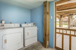 A laundry area with two white washers and dryers, a wooden door frame, and a view through a glass door.