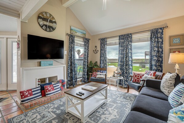 A living room with a fireplace, a television, and a view of the outdoors. - Walk to Matagorda Beach! Condo w/ Pool Access (Matagorda)