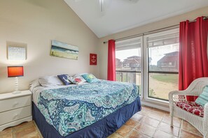 A bedroom with a bed, a nightstand, a window with curtains, a chair, and a view of a house. - Walk to Matagorda Beach! Condo w/ Pool Access (Matagorda)