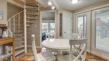 Un coin repas avec une table ronde, des chaises blanches, un escalier et une vue à travers une porte vitrée.