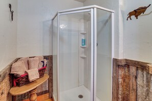 Een douche met glazen deur, een houten plank met handdoeken, en een rustieke muur.