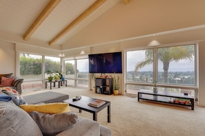 A spacious living room with a large TV, comfortable seating, and large windows offering a city view. - Ocean View + Private Garden: Santa Cruz Home (Santa Cruz)