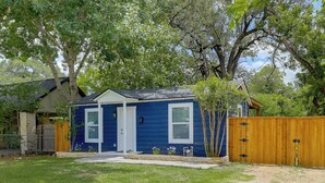 Una pequeña casa azul con porche, cerca de madera y un árbol al fondo.