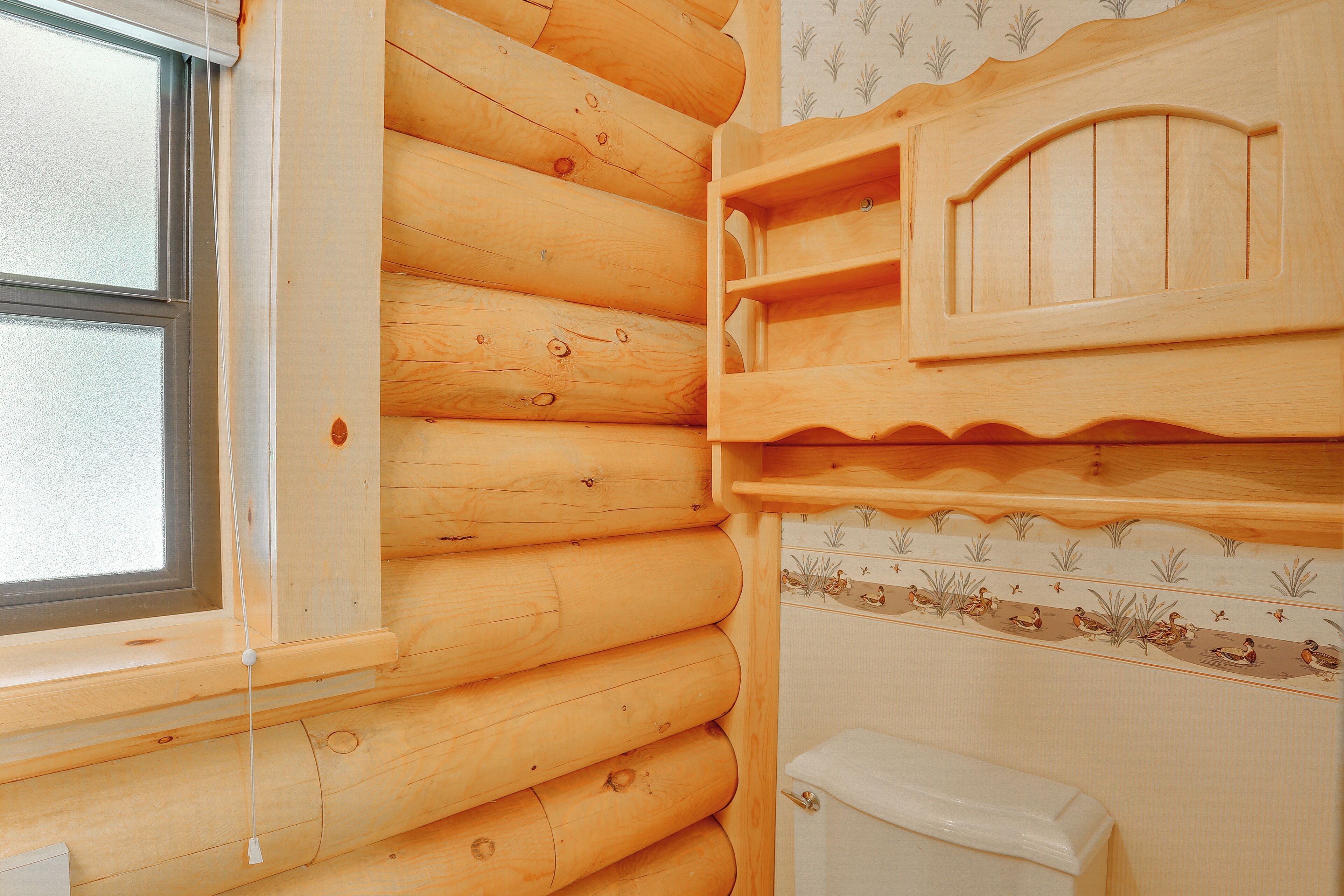 Ein rustikales Blockhaus-Interieur mit Fenster, Holzwänden, Toilette und dekorativer Regalfläche.