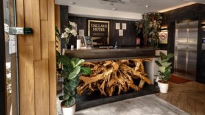 A reception desk with a sign reading 'ENCLAVE HOTEL,' a wooden wall, and potted plants. - Enclave Hotel Kuala Lumpur (Kuala Lumpur)