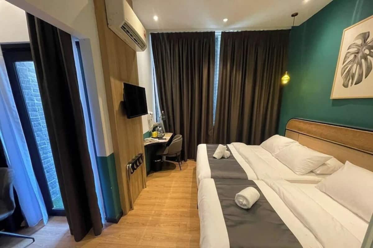 Ein Hotelzimmer mit Bett, Schreibtisch, Stuhl, Fernseher und einem Fenster mit Vorhängen.