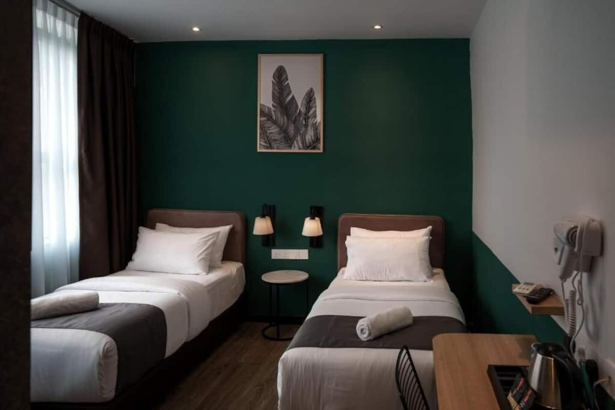 Ein Hotelzimmer mit zwei Betten, einem kleinen Tisch, einer Lampe, einem Telefon und einem Gemälde an der Wand.